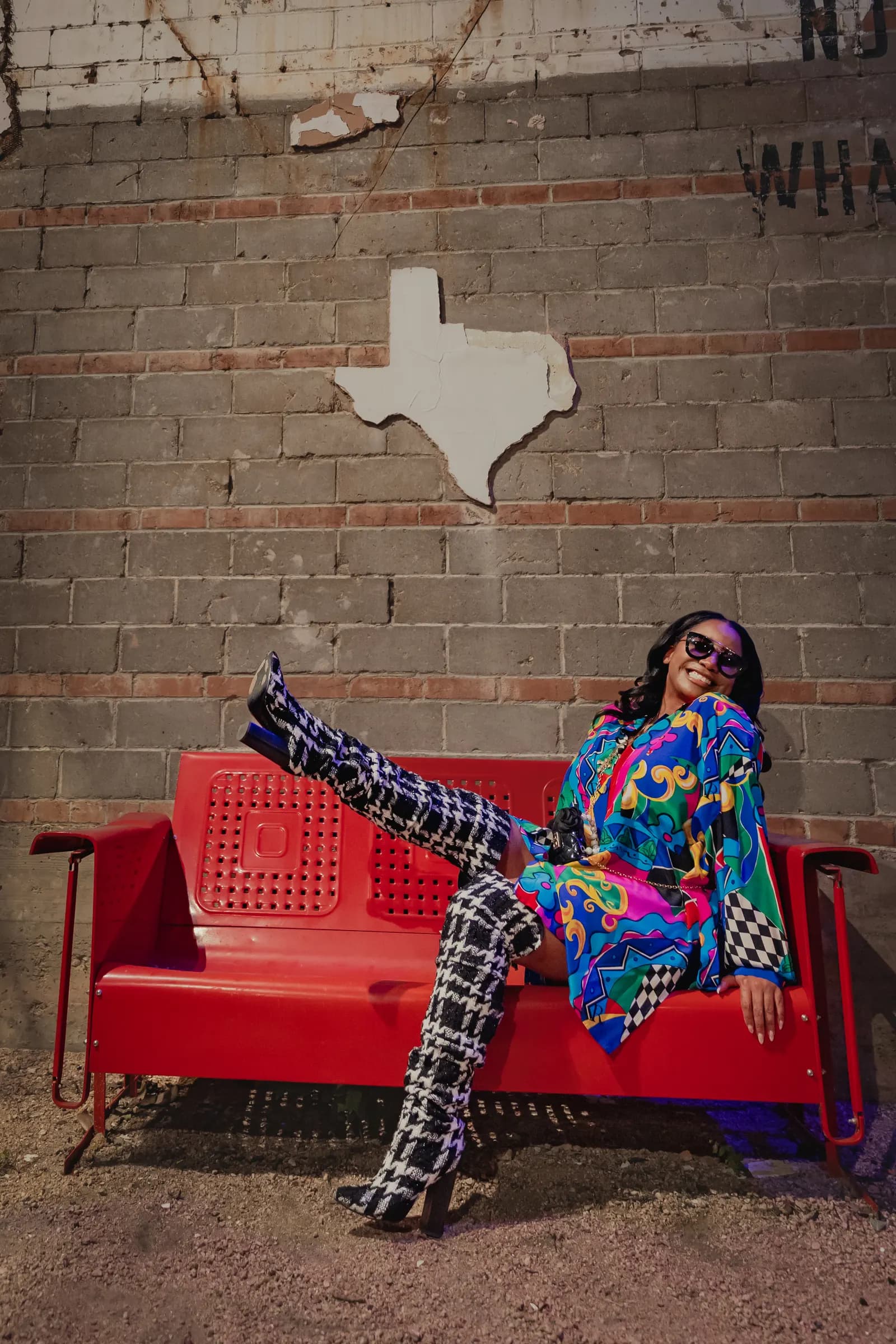 A creative in a bright patterned outfit striking a pose on a red bench